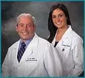 Portrait of two people standing side by side wearing white lab coats against a neutral background.